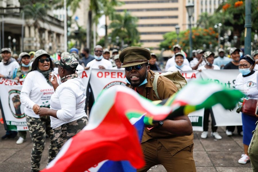 A member of Operation Dudula waves the South African national flag as others sing and chant anti-migrant slogans during their KwaZulu-Natal operation launch at Durban City Hall on April 10, 2022.